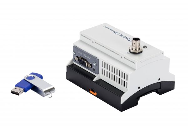 A compact white device with various ports, labeled "PHOENIX Bus Interface Profibus," is positioned upright and has a metallic connector at the top. To its left lies a silver and blue USB flash drive, partly open. The background is plain white.