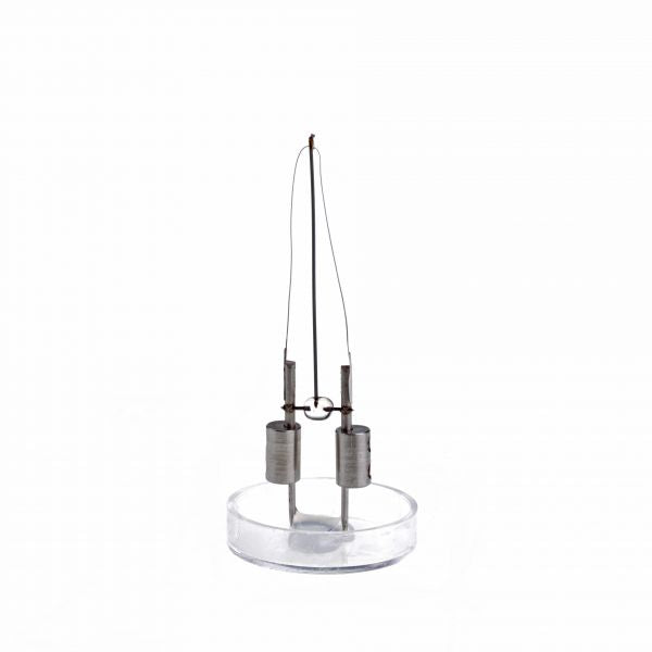 A delicate metal sculpture featuring two cylindrical weights hanging from thin wires, balanced on a clear round base. This piece, reminiscent of the precision associated with Leybold North America's Replacement Cathode for IE 413 / IE 414, showcases a modern, minimalist design.