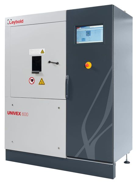 The image shows a Leybold North America HV-experimentation system UNIVEX 600, a piece of industrial equipment. It has a grey and dark grey exterior, a small display screen, and various warning symbols on the front panel. There is also a prominent red emergency stop button next to the screen.