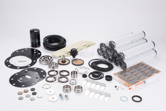 An assortment of mechanical components from the Repair Kit SV630-SV630 F by Leybold North America is displayed on a white background. The collection includes cylindrical parts, circular disks with holes, washers, bearings, and various metallic and plastic pieces. Some elements are recognizable as maintenance and repair equipment.
