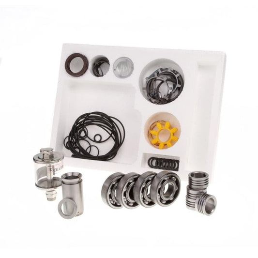 An array of mechanical components organized in a white foam tray. The parts include several metal rings, black O-rings, a metallic chamber with a clear casing, a yellow star-shaped piece, and other small metal and plastic pieces from the Major Maintenance Kit WA 251 by Leybold.